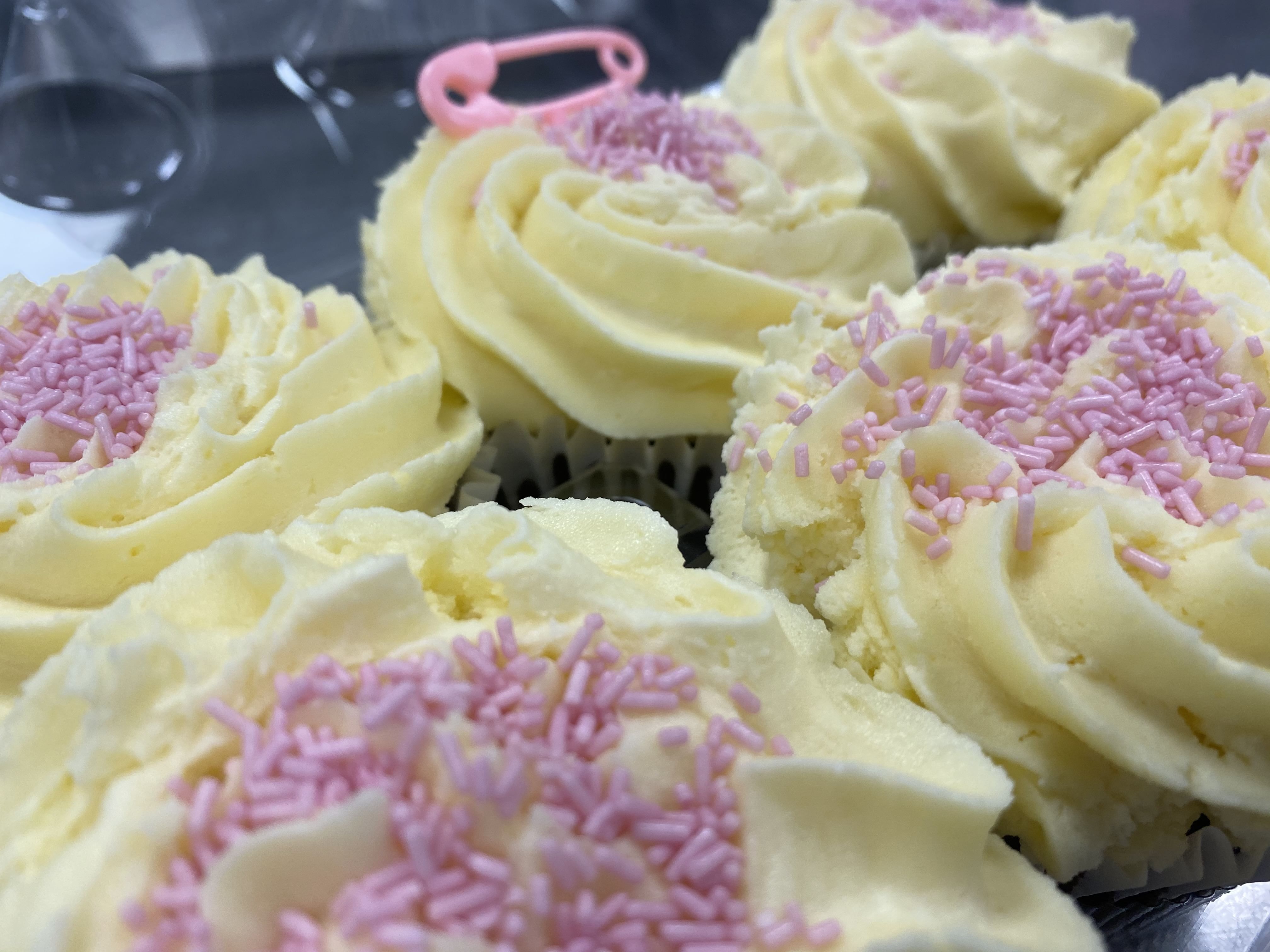 Close-up of vanilla cupcakes topped with swirls of creamy vanilla buttercream frosting and pink sprinkles. The cupcakes are arranged closely together, creating a visually appealing and delicious display of this timeless recipe.